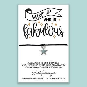 May include: A black string bracelet with a silver star charm. The card reads "Wake up and be fabulous" with gold stars and the text "Make a wish, tie on the bracelet when the thread wears thin & breaks away your wish will come true, so they say." The card also includes the company name "Wish Strings" and the website address "www.wishstrings.co.uk".