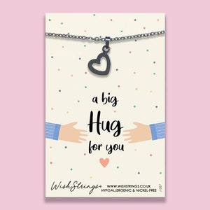 May include: A silver necklace with a heart charm and the text "a big Hug for you". The necklace is on a white card with a confetti pattern.