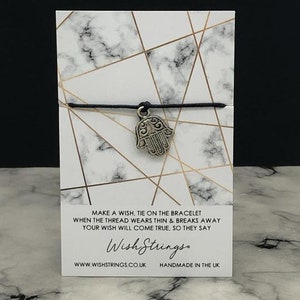 May include: Black string bracelet with a silver Hamsa hand charm. The card reads "Make a wish, tie on the bracelet when the thread wears thin & breaks away your wish will come true, so they say. Wish Strings. www.wishstrings.co.uk Handmade in the UK."