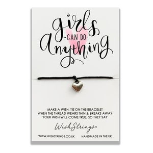 May include: Black string bracelet with a silver heart charm. The card reads "girls can do anything" with a pink heart and "Wish Strings" with the website and "Handmade in the UK".
