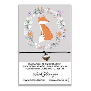 May include: A black string bracelet with a silver heart charm and a fox illustration with a floral wreath. The bracelet has the text "Make a wish, tie on the bracelet when the thread wears thin & breaks away your wish will come true, so they say" and "Wish Strings. WWW.WISHSTRINGS.CO.UK HANDMADE IN THE UK WS274".
