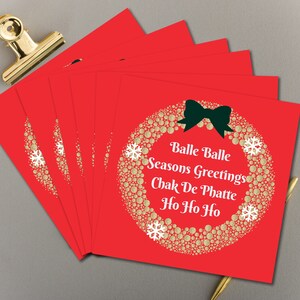 May include: A set of six red Christmas cards with a gold glitter wreath and a green bow. The cards have the text "Balle Balle Seasons Greetings Chak De Phatte Ho Ho Ho" printed on them.