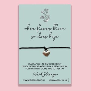 May include: A black string bracelet with a silver heart charm. The card reads "where flowers bloom so does hope" and "Make a wish, tie on the bracelet when the thread wears thin & breaks away your wish will come true, so they say." The card also includes the brand name "Wish Strings" and the website address "www.wishstrings.co.uk".