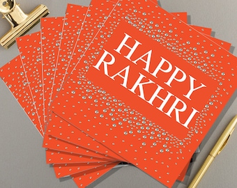 May include: A stack of orange greeting cards with silver glitter accents. The cards say "Happy Rakhri" in white text.