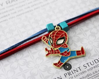 May include: A Spider-Man charm bracelet with a red, blue, and gold color scheme. The charm features a cartoon Spider-Man figure. The bracelet has a blue and red cord with turquoise beads. The background has text that reads "Y RAKSHA".