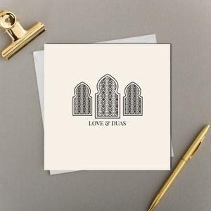 Puede incluir: Una tarjeta blanca con tres arcos negros delineados con diseños intrincados en su interior. El texto "LOVE & DUAS" está impreso debajo de los arcos.