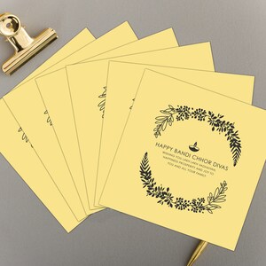 May include: A stack of yellow greeting cards with a black floral design and the text "HAPPY BANDI CHHOR DIVAS WISHING YOU LAIKH LAKH VADHAMAN, HAPPINESS PROSPERITY AND JOY TO YOU AND ALL YOUR FAMILY."