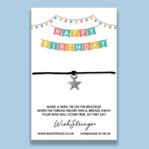 May include: A white card with a colorful banner that reads "Happy Birthday". The card also features a black string bracelet with a silver star charm. The text "Make a wish, tie on the bracelet when the thread wears thin & breaks away your wish will come true, so they say" is printed on the card. The text "Wish Strings" is printed in a stylized font. The text "www.wishstrings.co.uk Handmade in the UK" is printed at the bottom of the card.