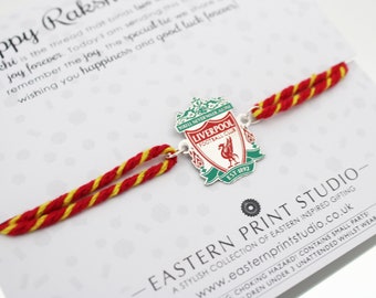 May include: A Liverpool Football Club enamel charm attached to a red and yellow twisted thread bracelet. The charm features the club crest with red, white, and green colors, including the text You'll Never Walk Alone and Est 1892.