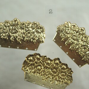 May include: Three gold-colored metal decorative pieces. Each piece features a rectangular basket shape with a textured wooden appearance, filled with a detailed floral design. The pieces have small holes along the bottom edge.