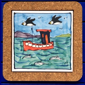 May include: A hand-painted ceramic tile featuring a red boat with white portholes sailing on a blue sea with white-capped waves. Two black birds with white beaks fly above the boat. The tile has a blue border and is set in a cork frame.