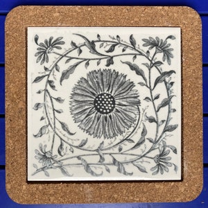 May include: A white ceramic tile with a black and white floral design. The design features a large flower in the centre surrounded by smaller flowers and leaves.