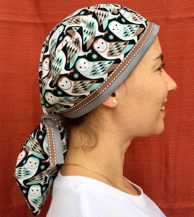 Puede incluir: Un gorro quir&uacute;rgico estampado en azul y marr&oacute;n con un dise&ntilde;o de b&uacute;ho blanco. El gorro tiene un ribete de cinta marr&oacute;n y se ata en la parte posterior.