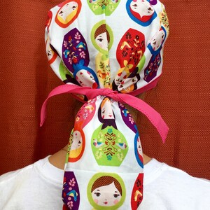 Puede incluir: Un gorro quir&uacute;rgico blanco con una cinta rosa, con un patr&oacute;n repetido de coloridas mu&ntilde;ecas rusas.