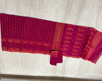 May include: A maroon and orange patterned saree with white polka dots. The saree is made of a thin, sheer fabric and has a border of orange and white stripes.