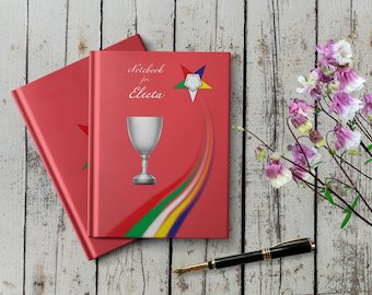 May include: Two red notebooks with the text "Notebook for Electa" on the front cover. The notebook on top has a silver chalice and a rainbow-colored star with a white five-pointed star in the center. The notebook on the bottom has a red star on the front cover.