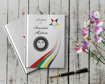 May include: White notebook with the text "Notebook for Associate Matron" and a five-pointed star with a sun symbol. The notebook is on a white wooden surface with pink flowers.