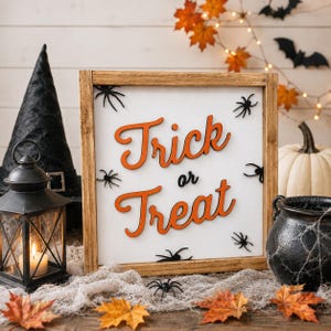 Puede incluir: Un letrero cuadrado de madera con fondo blanco que presenta el texto naranja en 3D Trick or Treat y varios recortes de arañas negras. El letrero está enmarcado en madera natural y muestra un tema festivo de Halloween con arañas dispersas.