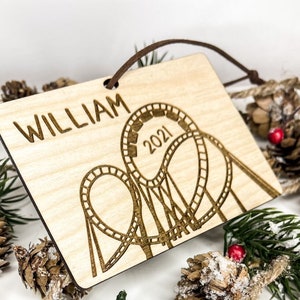 May include: Wooden Christmas ornament with a roller coaster design and the year 2021 engraved. The ornament is personalized with the name "William".