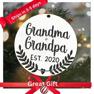 May include: White round Christmas ornament with black text that reads "Grandma + Grandpa EST. 2020" with a black wreath design around the text.