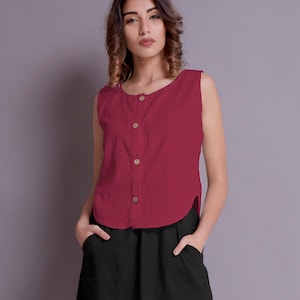 Puede incluir: Una mujer lleva una blusa sin mangas de color granate con botones en la parte delantera y una falda negra de línea A. Lleva sandalias de tacón beige.