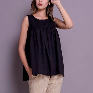 May include: A woman wearing a black sleeveless top with a gathered neckline and beige striped trousers. She is wearing white sandals.