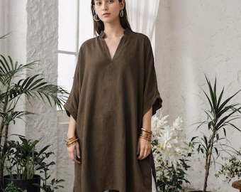 May include: A woman wearing a dark olive-green tunic top with a V-neck and short sleeves, paired with white cropped pants. She is wearing gold bracelets and earrings. The outfit is casual and comfortable.