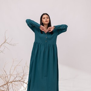 May include: A teal blue long-sleeved dress with a button-up front and a gathered skirt. The dress has a relaxed fit and is made of a lightweight fabric.