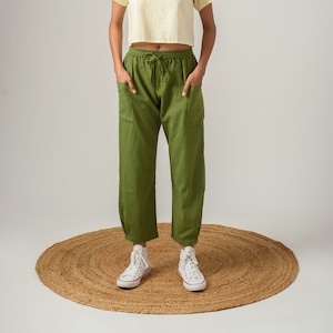 K&ouml;nnte beinhalten: Eine Frau tr&auml;gt ein hellgelbes, bauchfreies T-Shirt und eine olivgr&uuml;ne Hose mit Kordelzug. Sie steht auf einem runden gewebten Teppich und tr&auml;gt wei&szlig;e High-Top-Sneaker.