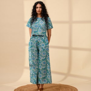 May include: A woman wearing a green and blue floral print crop top and matching wide-leg trousers. The outfit is made of cotton and has a relaxed fit.