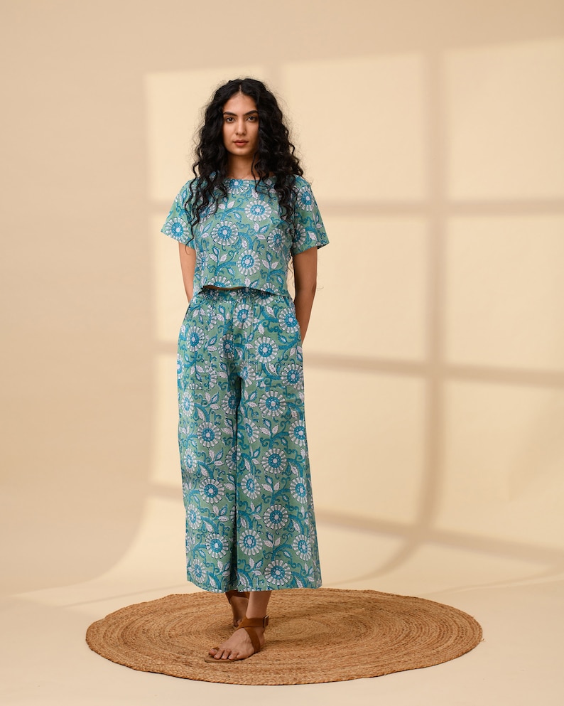 May include: A woman wearing a green and blue floral print crop top and matching wide-leg trousers. The outfit is made of cotton and has a relaxed fit.