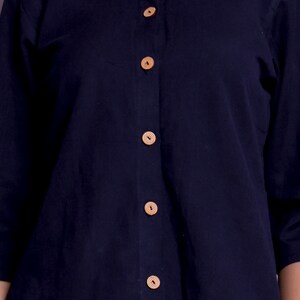 Pu&ograve; includere: Una camicia blu navy con colletto e chiusura con bottoni sul davanti e bottoni in legno.