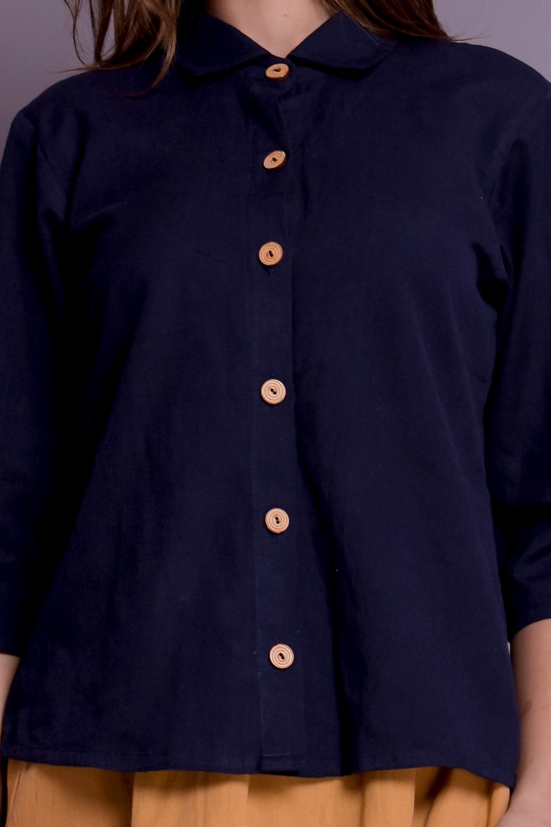 Pu&ograve; includere: Una camicia blu navy con colletto e chiusura con bottoni sul davanti e bottoni in legno.