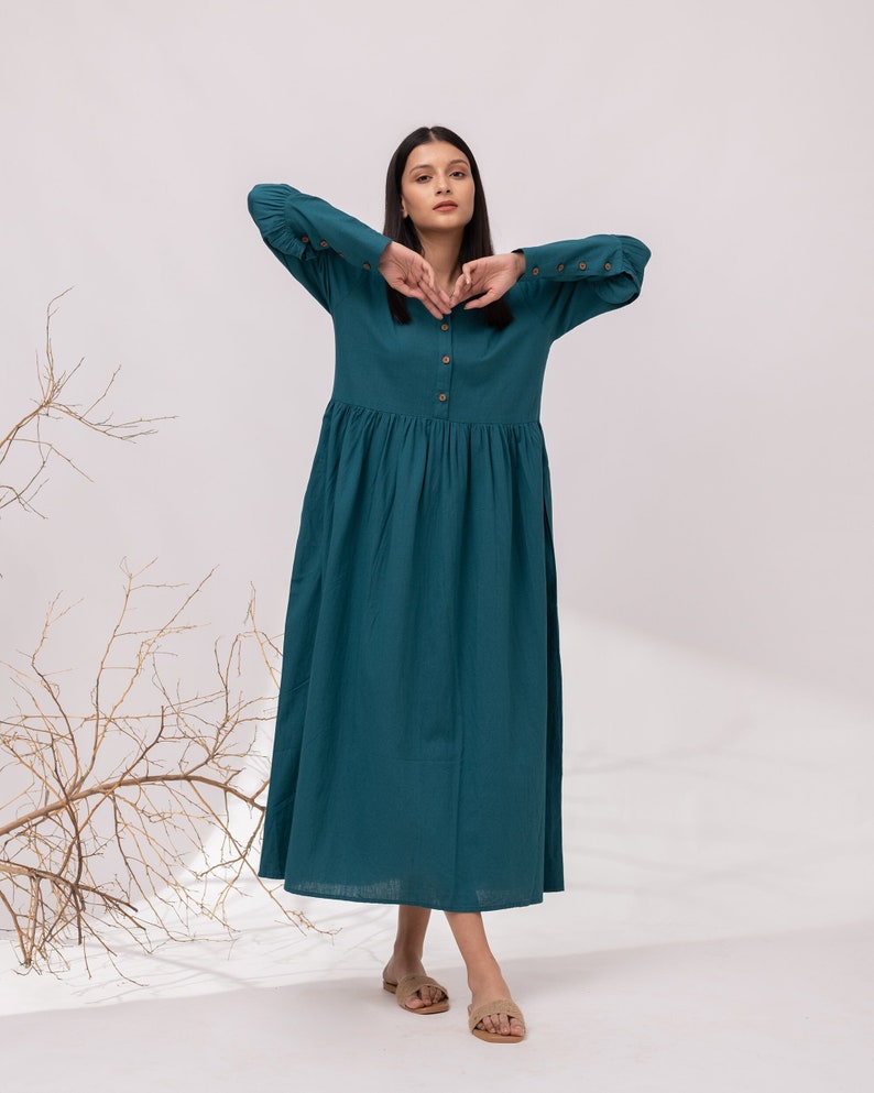 May include: A teal blue long-sleeved dress with a button-up front and a gathered skirt. The dress has a relaxed fit and is made of a lightweight fabric.
