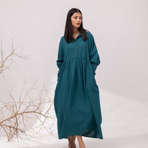 May include: A teal blue long-sleeved dress with a button-up front and a gathered skirt. The dress is made of a lightweight fabric and has a relaxed fit.