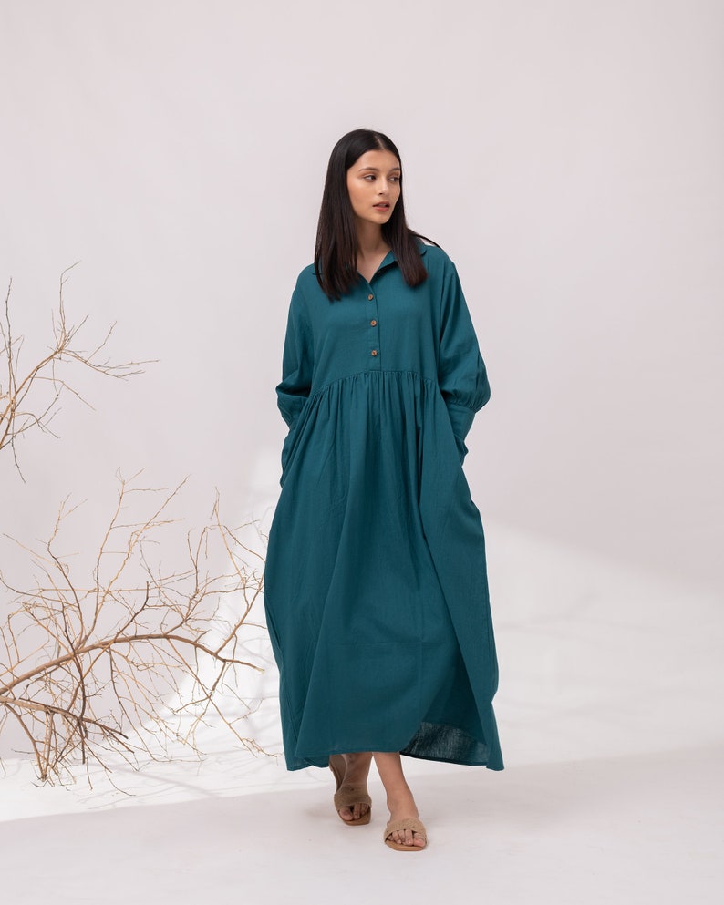 May include: A teal blue long-sleeved dress with a button-up front and a gathered skirt. The dress is made of a lightweight fabric and has a relaxed fit.