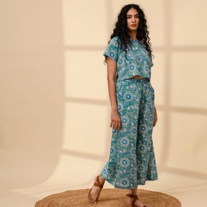 May include: A teal blue and white floral print crop top and wide-leg trousers set. The top has short sleeves and a round neckline. The trousers have a wide leg and a relaxed fit.