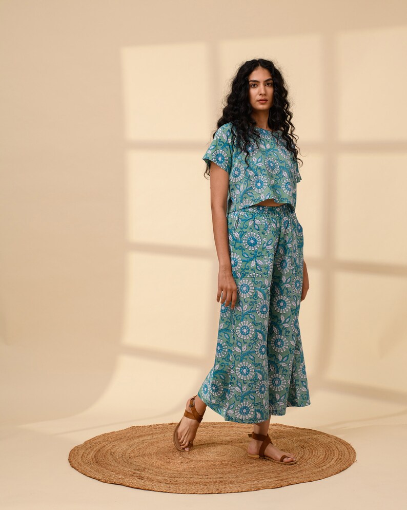 May include: A teal blue and white floral print crop top and wide-leg trousers set. The top has short sleeves and a round neckline. The trousers have a wide leg and a relaxed fit.