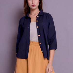 Pu&ograve; includere: Una camicia blu navy con bottoni, maniche lunghe e una gonna color senape. La camicia ha bottoni in legno.
