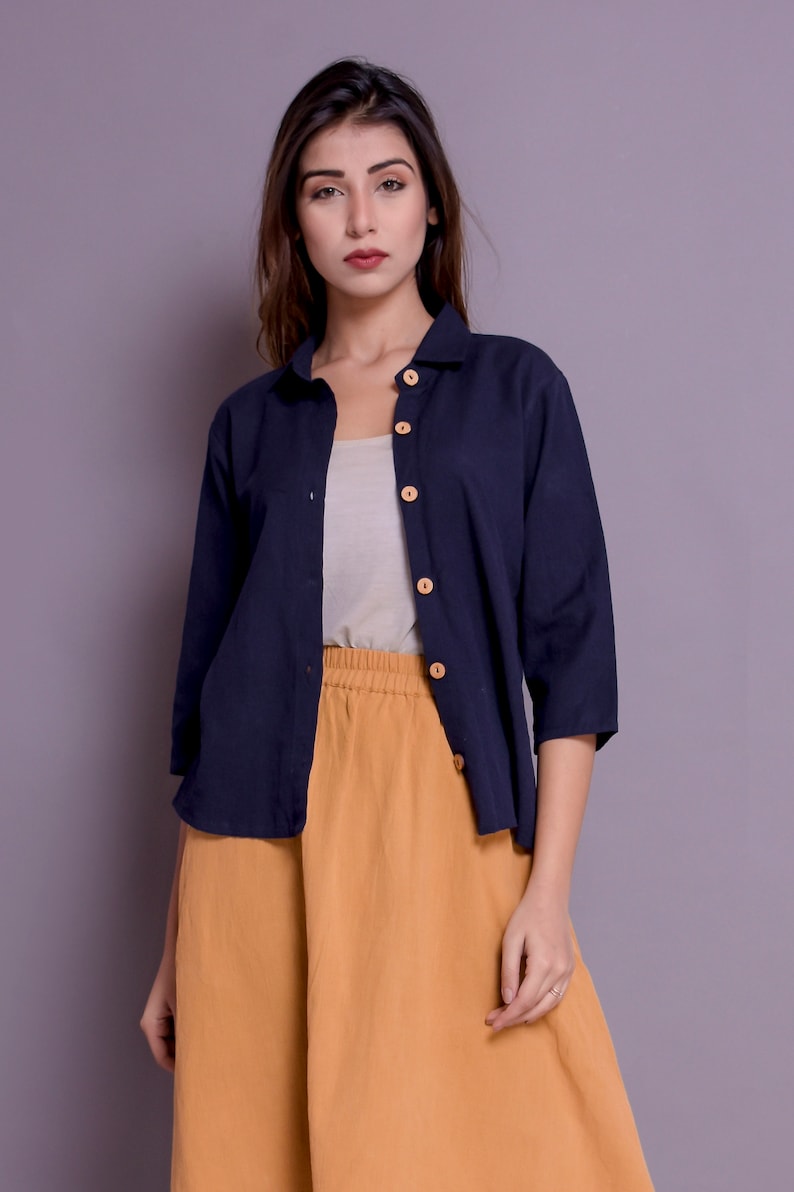 Pu&ograve; includere: Una camicia blu navy con bottoni, maniche lunghe e una gonna color senape. La camicia ha bottoni in legno.