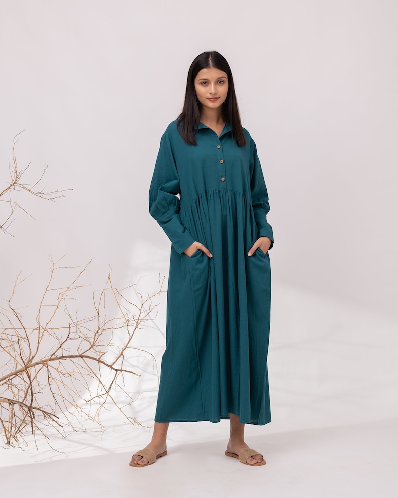 May include: A teal blue long-sleeved collared dress with pockets. The dress has a gathered waist and a relaxed fit.