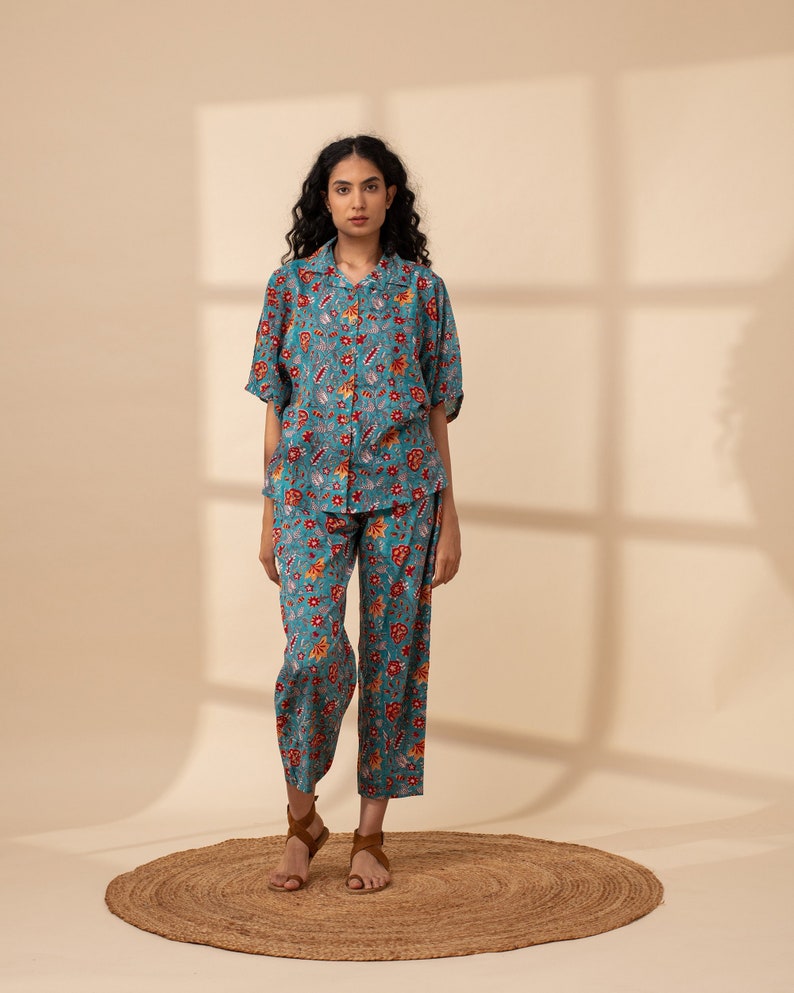 May include: A teal blue pyjama set with a floral print in shades of red, orange, and yellow. The set includes a short-sleeved shirt with a collared neckline and matching trousers.