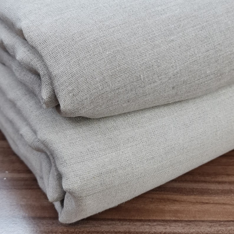 May include: Two pieces of light gray fabric folded together. The fabric has a woven texture.