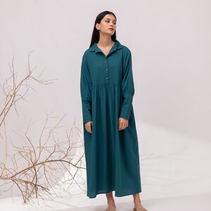 May include: A teal blue long-sleeved dress with a collared neckline and button closure. The dress has a gathered skirt and is made of a lightweight fabric.
