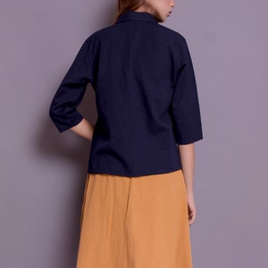 Pu&ograve; includere: Una donna indossa una camicia blu navy a tre quarti con colletto e una gonna giallo senape.