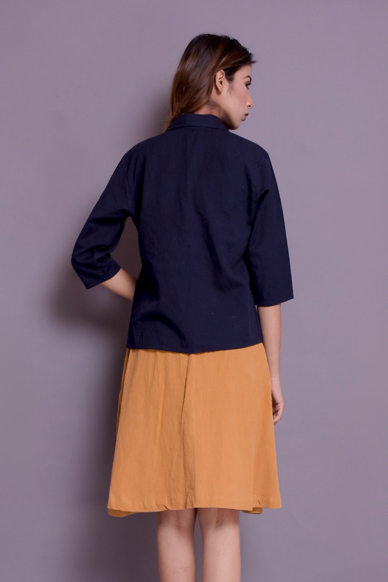 Pu&ograve; includere: Una donna indossa una camicia blu navy a tre quarti con colletto e una gonna giallo senape.