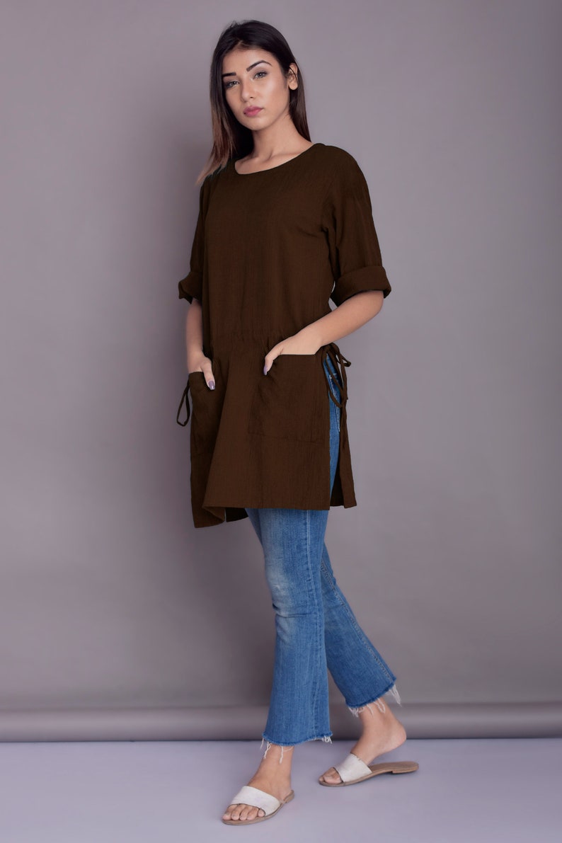 May include: A brown linen tunic with side slits and pockets. The tunic is worn with blue jeans and white sandals.