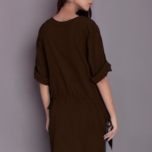 May include: A brown, long-sleeved tunic with a drawstring waist and side slits. The tunic is made of a soft, comfortable fabric and has a relaxed fit.
