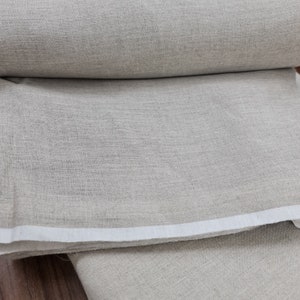 May include: A close-up of a roll of natural linen fabric. The fabric is a light beige color and has a slightly textured surface.