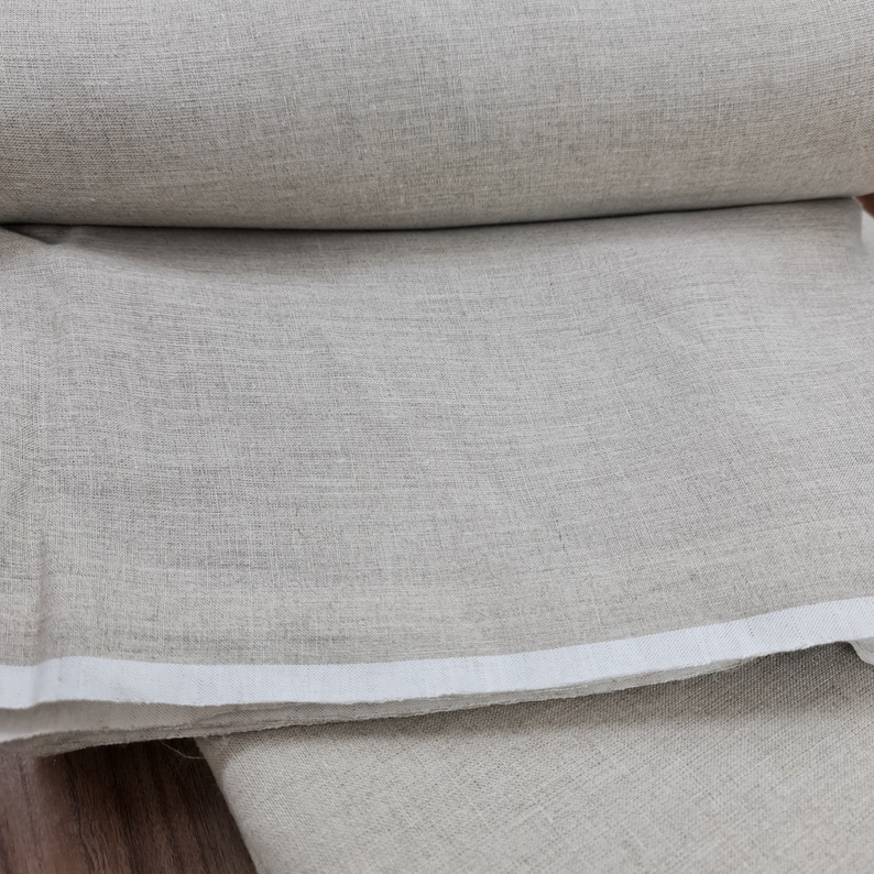 May include: A close-up of a roll of natural linen fabric. The fabric is a light beige color and has a slightly textured surface.